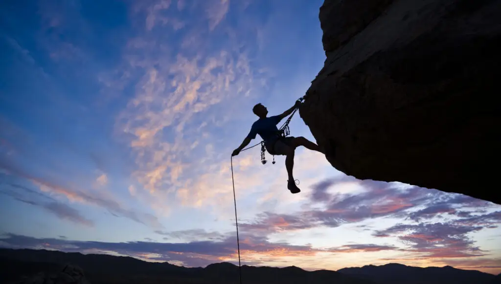 rock climber at outcrop securely roped to climb higher
