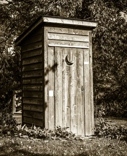 old wooden privy outhouse at edge of woods